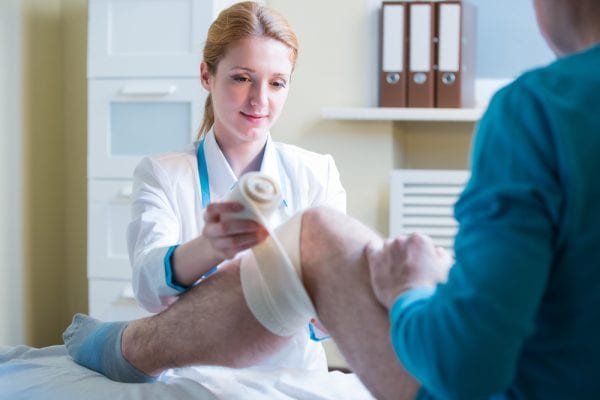 Female doctor wrapping a middle age man's knee